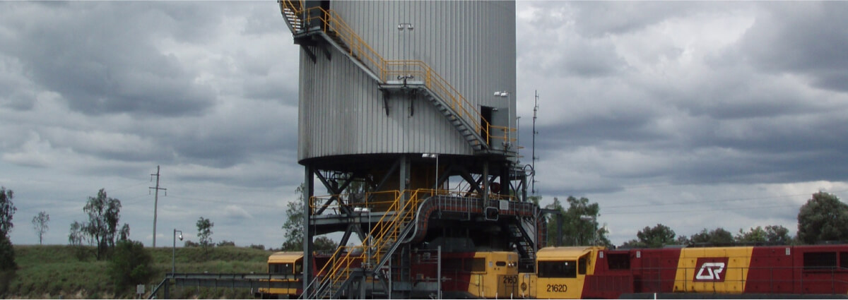 A large industrial structure with multiple staircases and a train underneath, set against a cloudy sky, illustrating Hazardous Area Designs.