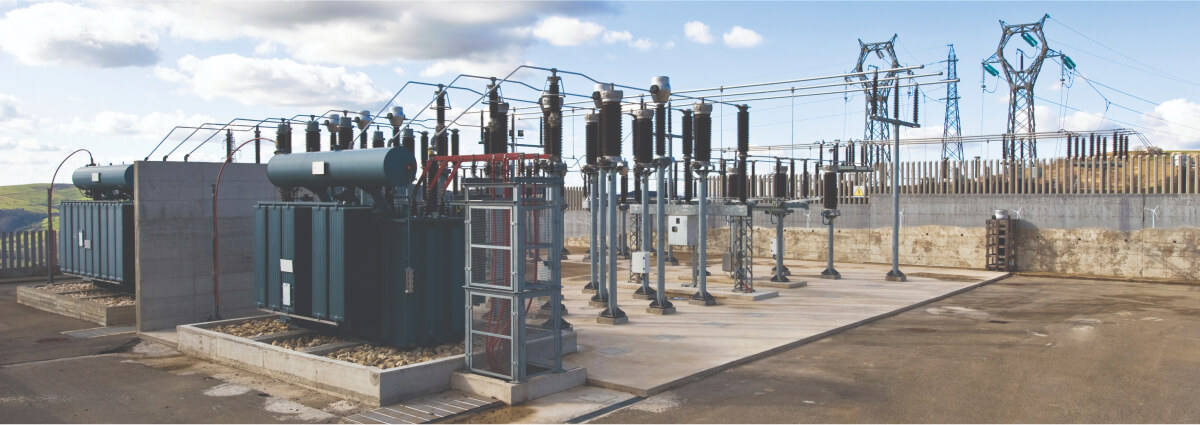 Electrical substation with transformers and high-voltage equipment under a partly cloudy sky, illustrating the infrastructure and technology involved in power distribution