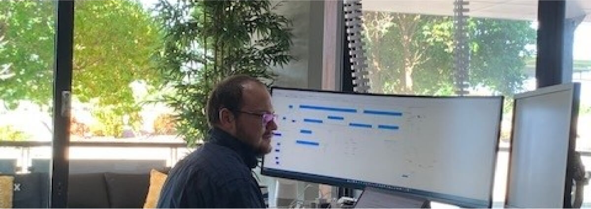 Engineer working at a desk with multiple computer monitors displaying project timelines and data, illustrating the detailed planning and management